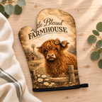 One Blessed Farmhouse Highland cow oven mitt with black trim, styled on pale timber with ivory linen and eucalyptus. Sold individually; decorative props not included.