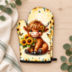 One Sunflower Highland cow oven mitt with black trim on pale timber beside ivory linen and eucalyptus. Sold individually; decorative props not included.