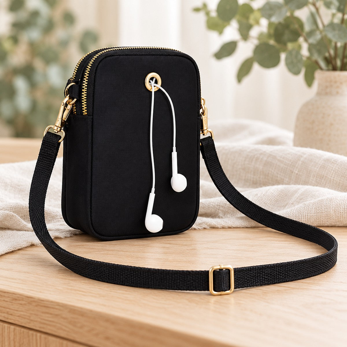 Back of the black mini crossbody bag showing the cable opening, detachable gold-tone clips and adjustable strap.