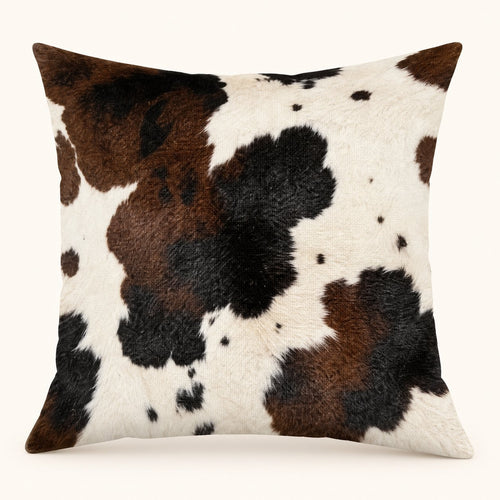 One cream cushion cover with large chocolate brown and black cow-print patches, shown filled; insert not included