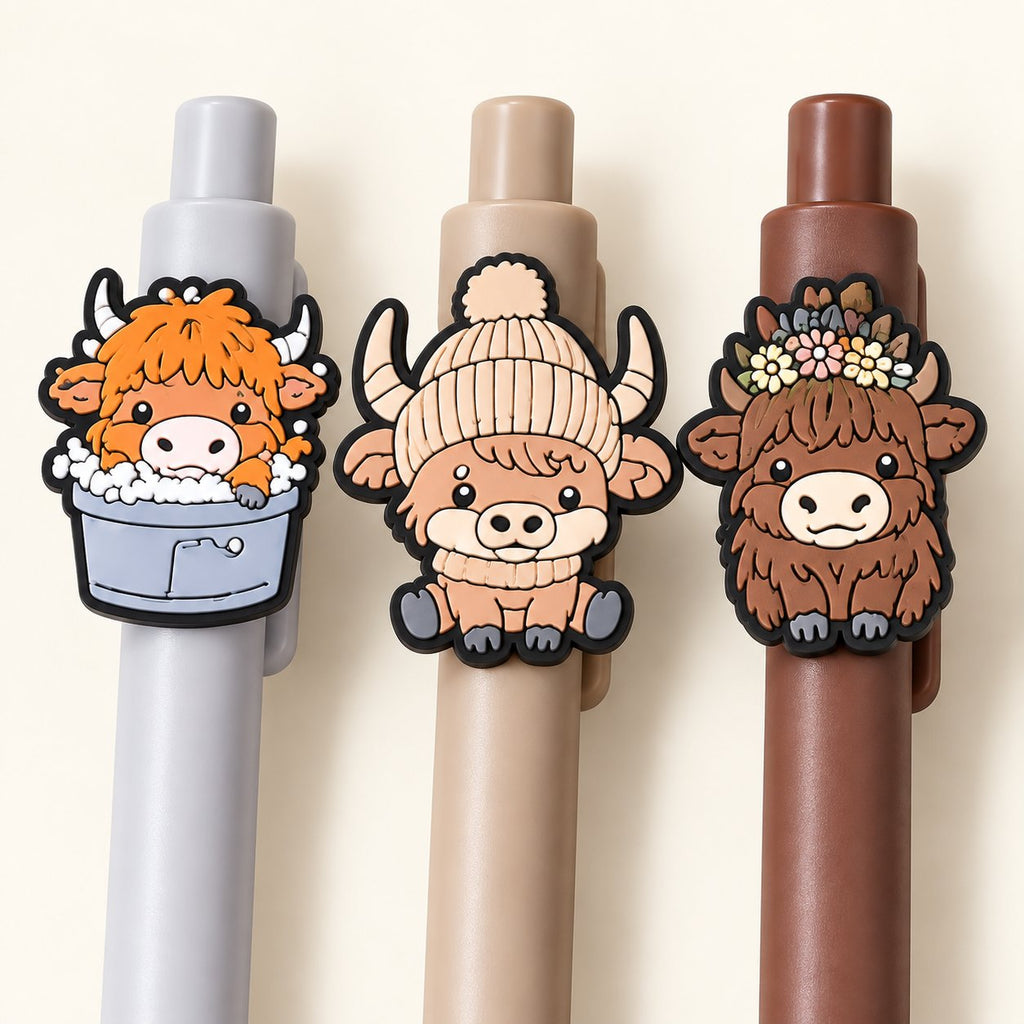Close-up of three Highland cow pen toppers showing assorted printed rubber designs