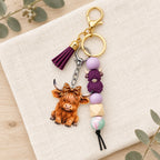 Purple Highland cow tassel keyring styled on cream linen with eucalyptus in the background
