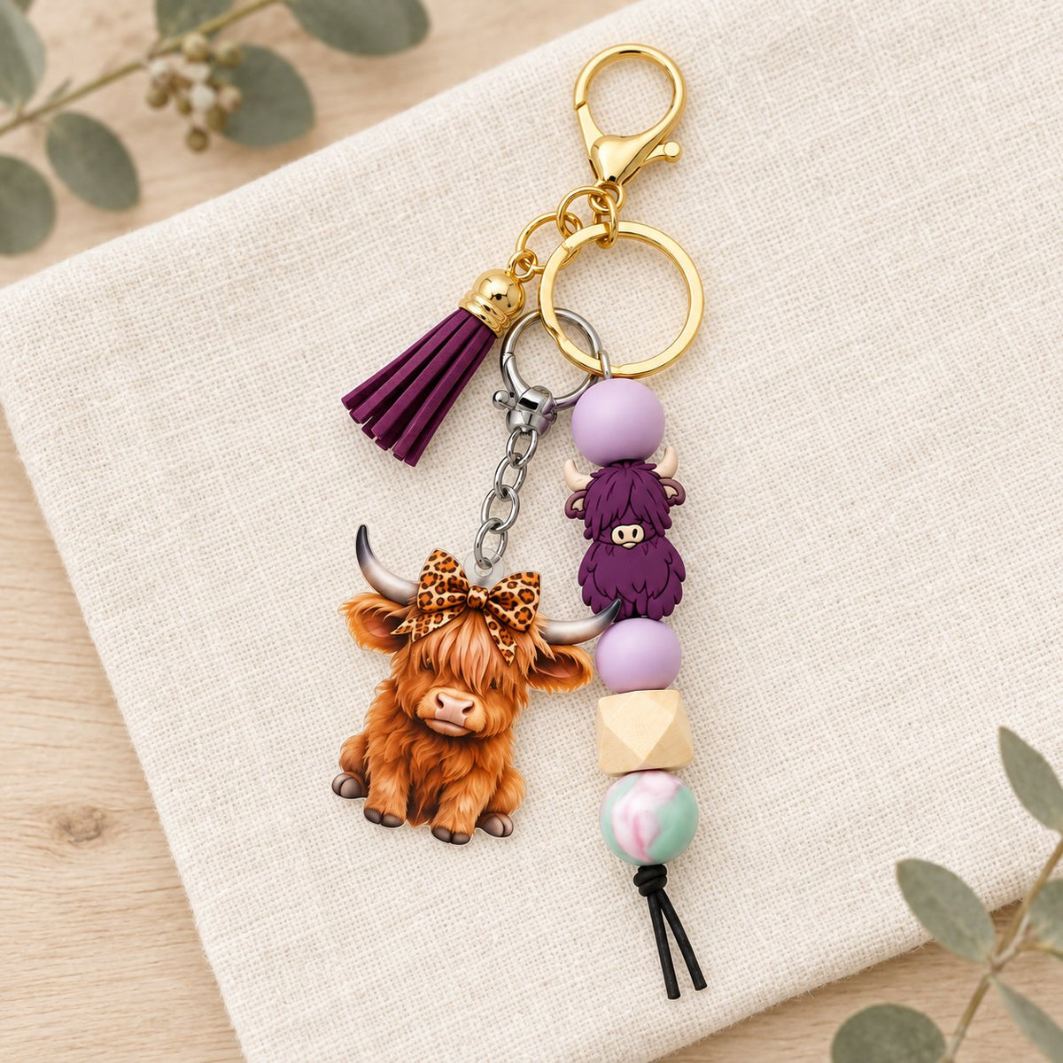 Purple Highland cow tassel keyring styled on cream linen with eucalyptus in the background