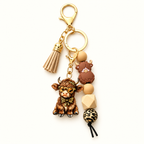 Brown Highland cow beaded tassel keyring with a cow charm, coordinating beads and gold-tone clasp, shown individually on an ivory background.