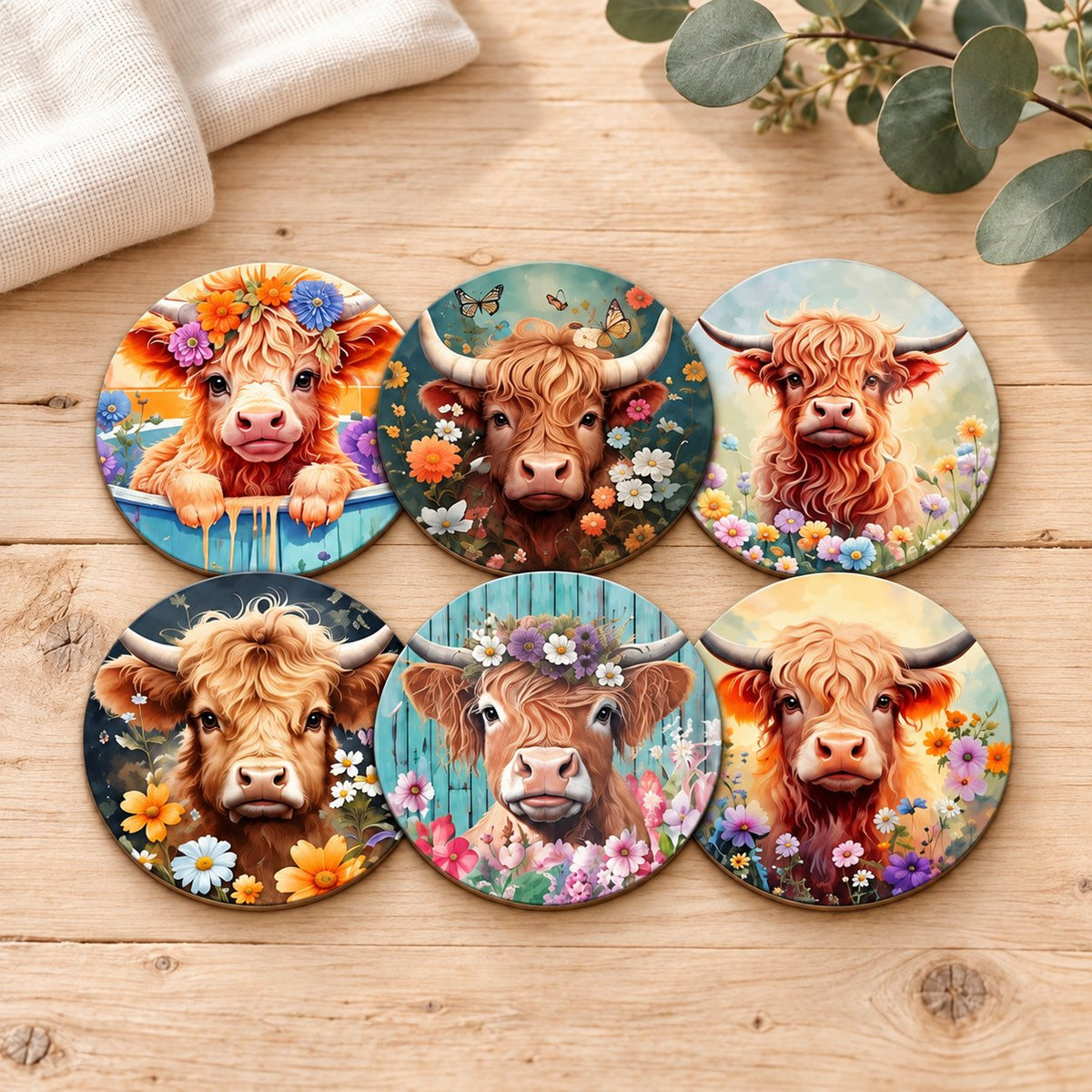 Six floral Highland cow coasters on pale timber with cream linen and eucalyptus; decorative props are not included.