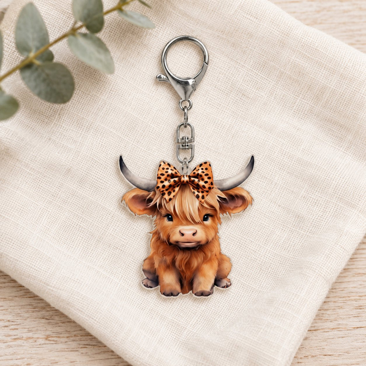 Leopard-bow Highland calf keyring on cream linen with decorative foliage; styling props are not included.