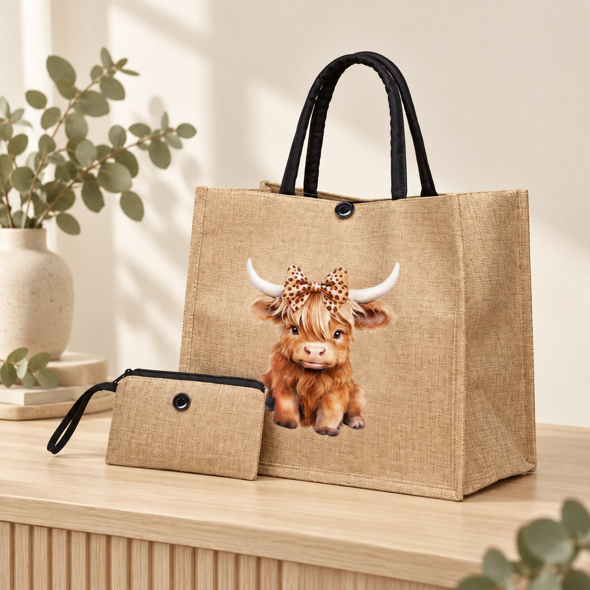 Styled view of a khaki Highland cow leopard-bow tote with black handles and coordinating plain purse on a timber surface; decorative props are not included.