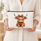 White Highland cow makeup pouch held by a woman in a cream linen shirt