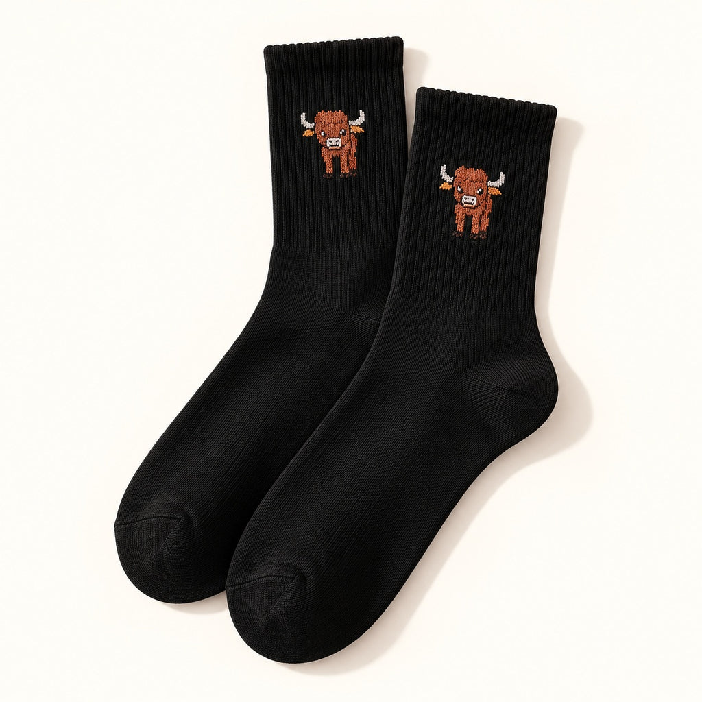 One pair of black Highland cow crew socks with a small cow motif, shown on an ivory background.