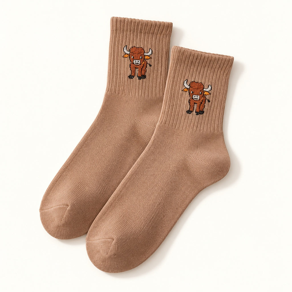 One pair of camel Highland cow socks with ribbed cuffs and a small cow motif, shown on an ivory background.