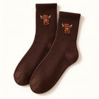 One pair of chocolate brown Highland cow socks with ribbed cuffs and a small cow motif, shown on an ivory background.