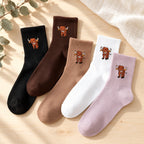 Highland cow socks in five colours styled on pale timber with linen and eucalyptus; each colour is sold by the pair.