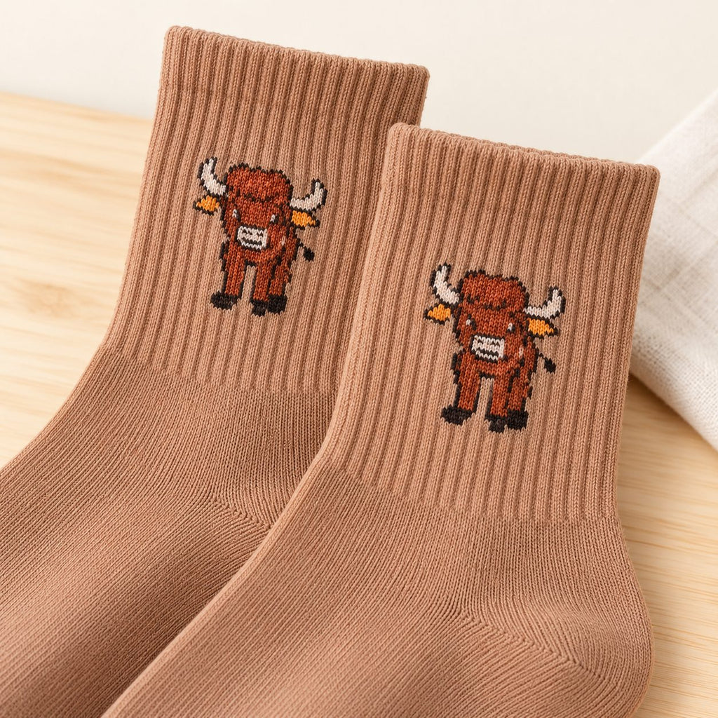 Close-up of camel Highland cow socks showing the knitted cow motif and ribbed cuffs.