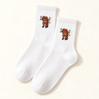 One pair of white Highland cow socks with ribbed cuffs and a small cow motif, shown on an ivory background.