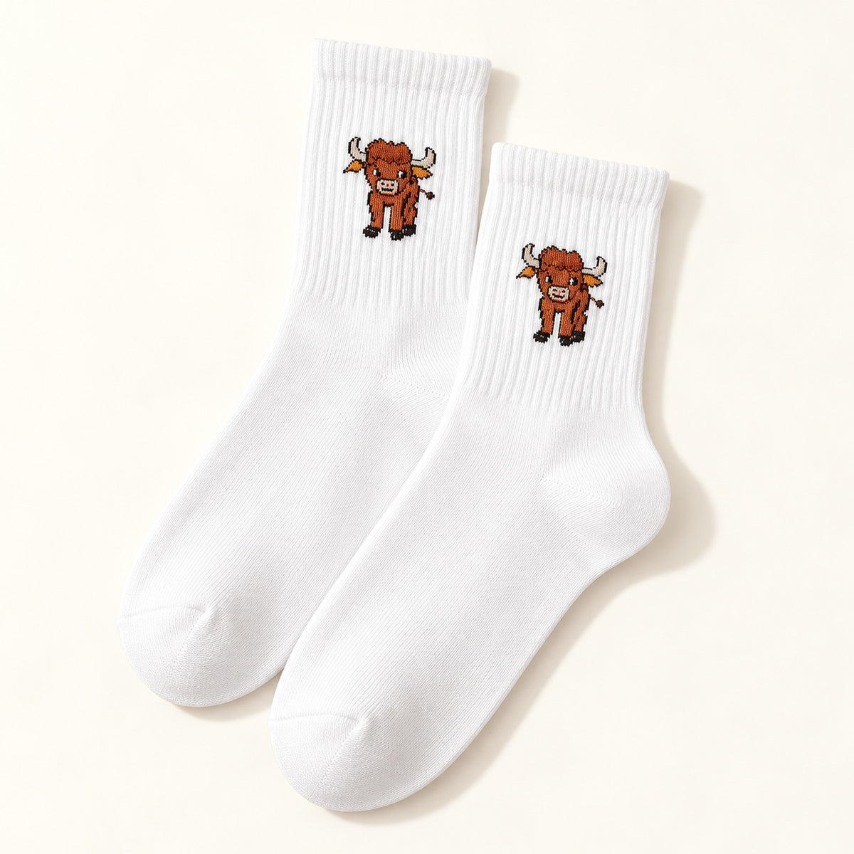 One pair of white Highland cow socks with ribbed cuffs and a small cow motif, shown on an ivory background.
