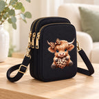 Leopard Bow Highland cow mini crossbody bag with three gold-tone zips, styled on an oak table in a warm neutral room.