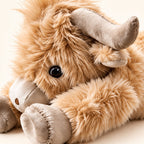 Close-up of the lying plush cow’s eye, curved horn, shaggy tan fur and stitched hoof