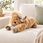 Lying Highland cow plush on a cream sofa with sage cushion; decorative props not included