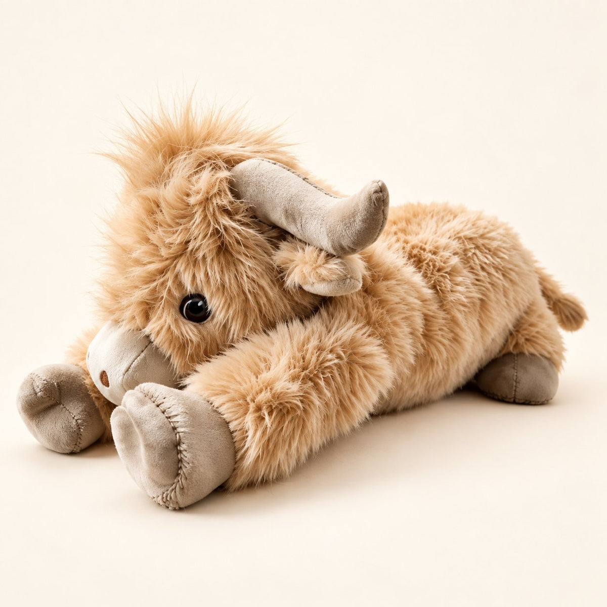 Tan Highland cow plush in a lying pose with curved taupe horns and stitched hoof pads