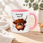 Pink Morning Moo Highland cow mug styled on pale timber with linen and greenery; decorative props not included.