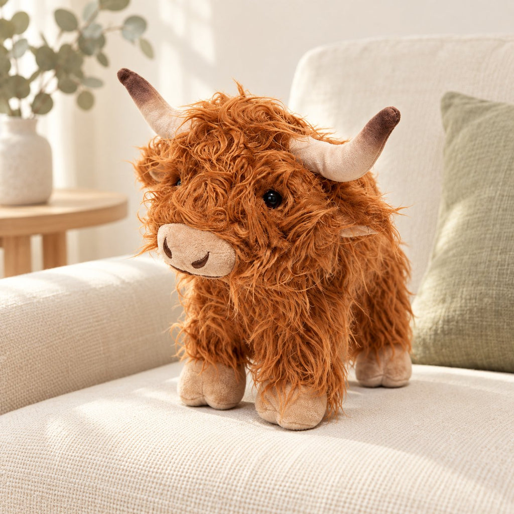 Brown standing Highland cow plush styled on a cream sofa; decorative props not included